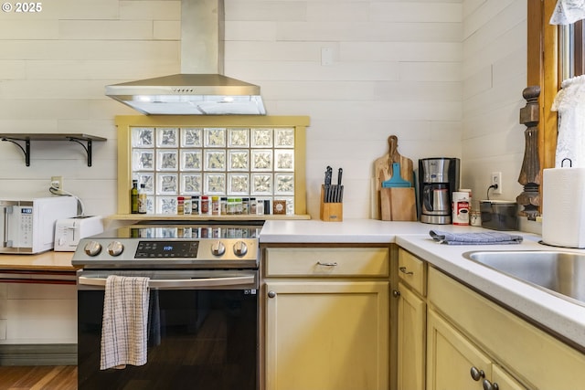 kitchen featuring range hood, wood-type flooring, wood walls, and stainless steel electric range