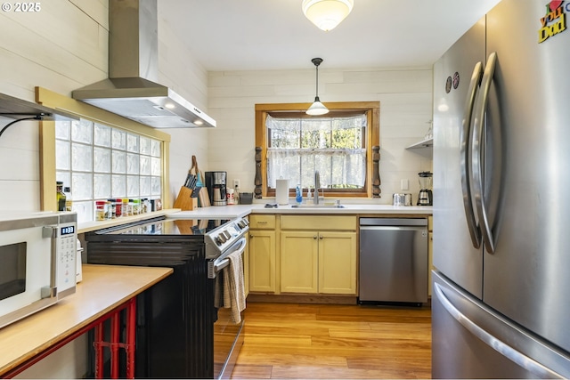 kitchen featuring pendant lighting, extractor fan, stainless steel appliances, sink, and light hardwood / wood-style flooring