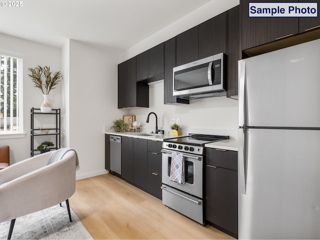10985 E Burnside St Unit 3, Portland, OR 97216 - kitchen featuring appliances with stainless steel finishes, a sink, light wood-style floors, light countertops, and dark cabinetry