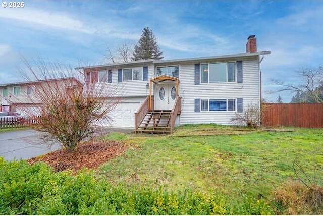 split foyer home with a garage, driveway, a chimney, fence, and a front yard