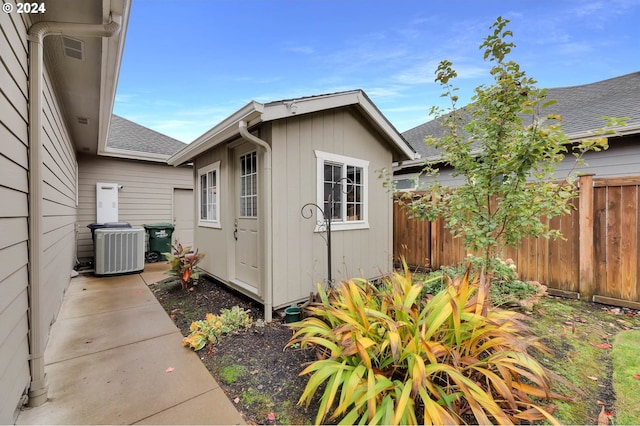 view of property exterior with an outbuilding, central AC unit, a shingled roof, and fence