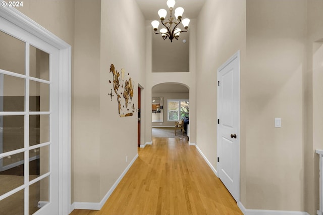 hallway featuring baseboards, arched walkways, a towering ceiling, light wood-type flooring, and a notable chandelier