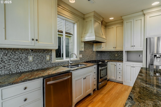 kitchen with stainless steel appliances, sink, custom exhaust hood, and dark stone counters