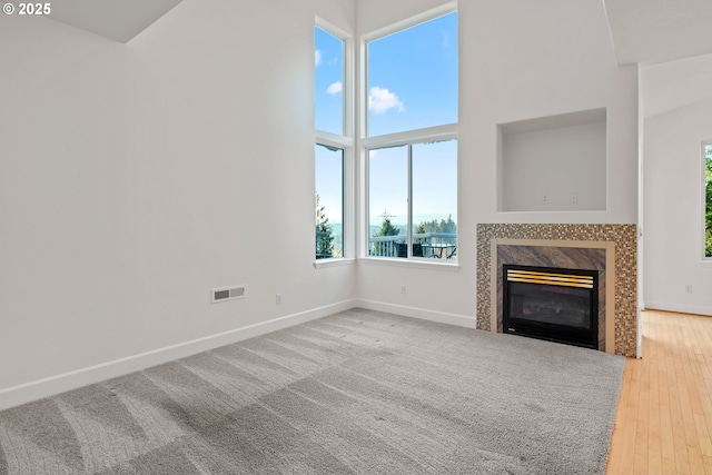 unfurnished living room featuring a high end fireplace, a towering ceiling, and wood-type flooring