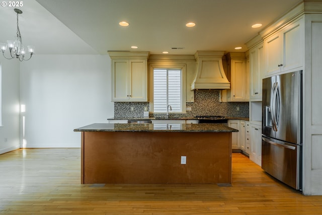 kitchen with stainless steel refrigerator with ice dispenser, a kitchen island, custom range hood, and decorative light fixtures