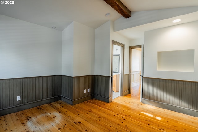 unfurnished room featuring vaulted ceiling with beams and light hardwood / wood-style flooring