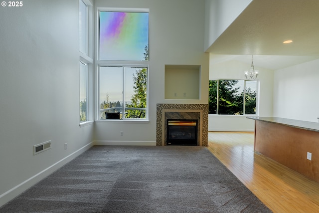 unfurnished living room featuring hardwood / wood-style flooring, a premium fireplace, a towering ceiling, and a chandelier