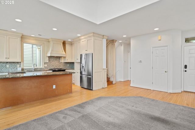 kitchen with light wood-type flooring, cream cabinets, custom range hood, stainless steel fridge, and sink