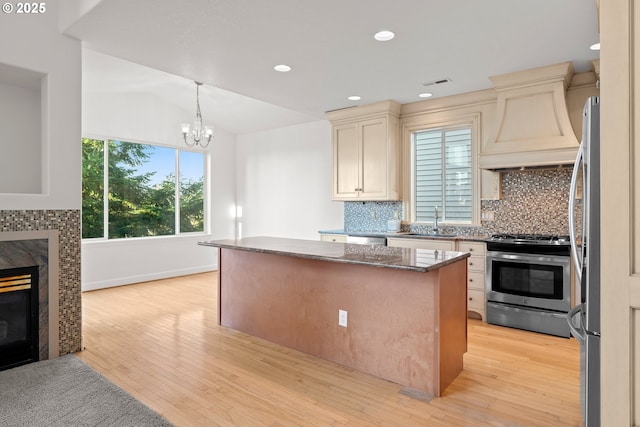 kitchen featuring appliances with stainless steel finishes, premium range hood, dark stone counters, a premium fireplace, and sink