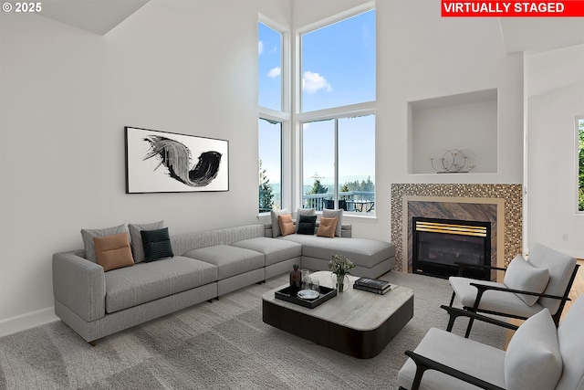 carpeted living room featuring a high end fireplace and a towering ceiling