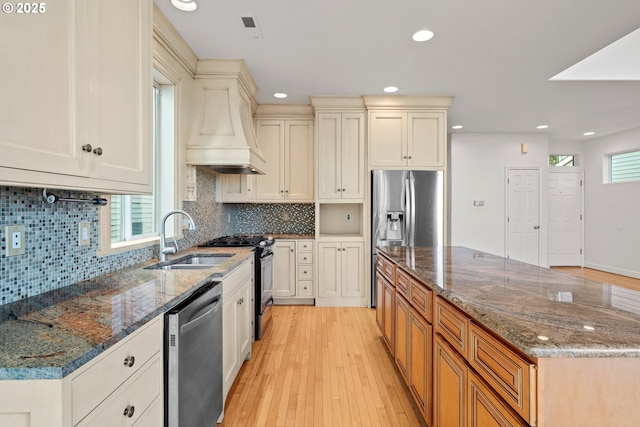 kitchen featuring stainless steel appliances, light hardwood / wood-style floors, premium range hood, sink, and dark stone counters