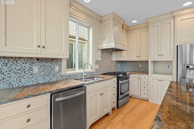 kitchen with sink, appliances with stainless steel finishes, custom exhaust hood, and dark stone counters