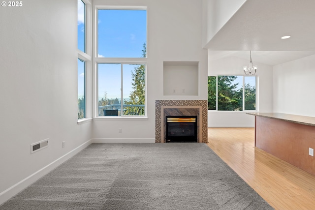 unfurnished living room with a notable chandelier, a towering ceiling, wood-type flooring, and a wealth of natural light