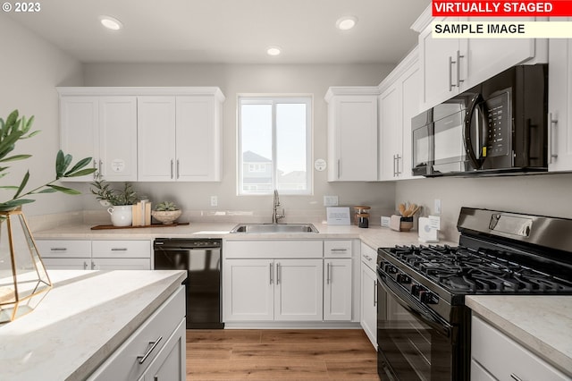 kitchen with a sink, black appliances, light wood-style flooring, and white cabinetry