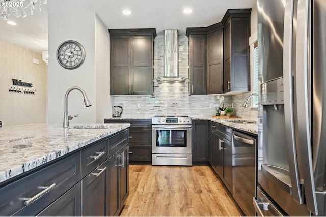 655 Schemmel Ln, Silverton, OR 97381 - kitchen featuring stainless steel appliances, wall chimney range hood, decorative backsplash, light stone countertops, and light wood-type flooring