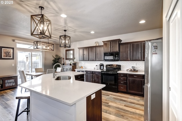 kitchen with a kitchen bar, sink, a center island with sink, hanging light fixtures, and black appliances