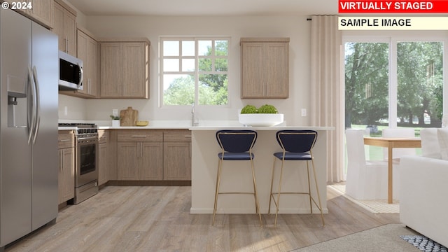 kitchen featuring a kitchen bar, appliances with stainless steel finishes, light brown cabinets, and light hardwood / wood-style floors