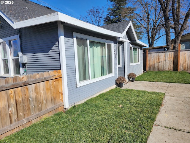 view of home's exterior featuring fence, a lawn, and roof with shingles