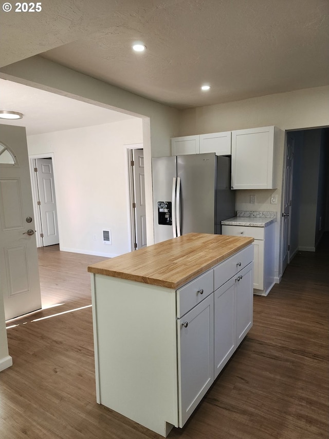 kitchen with a center island, stainless steel refrigerator with ice dispenser, visible vents, dark wood-type flooring, and white cabinetry