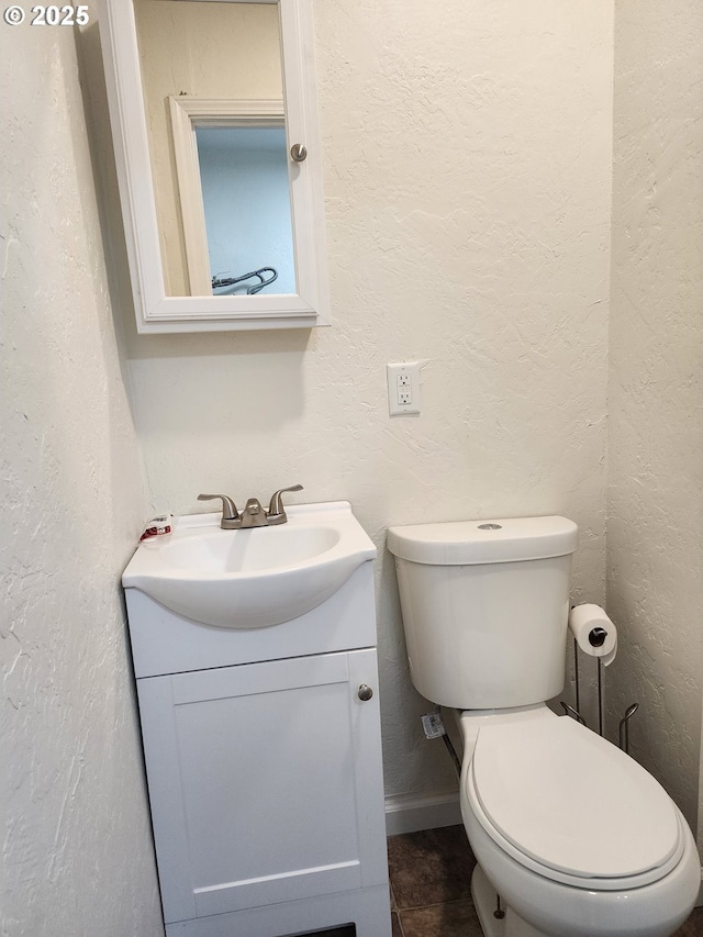 half bath featuring toilet, vanity, baseboards, and a textured wall