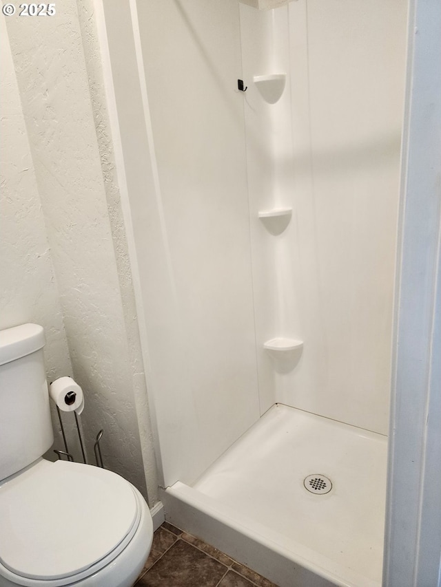 full bathroom featuring a textured wall, a stall shower, toilet, and tile patterned floors