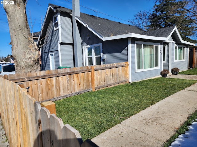 view of home's exterior featuring a chimney, fence, a lawn, and roof with shingles