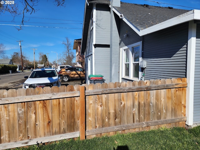 view of side of home with roof with shingles and fence