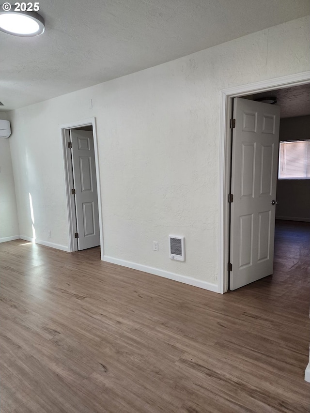 empty room featuring a textured ceiling, a wall mounted air conditioner, wood finished floors, and baseboards