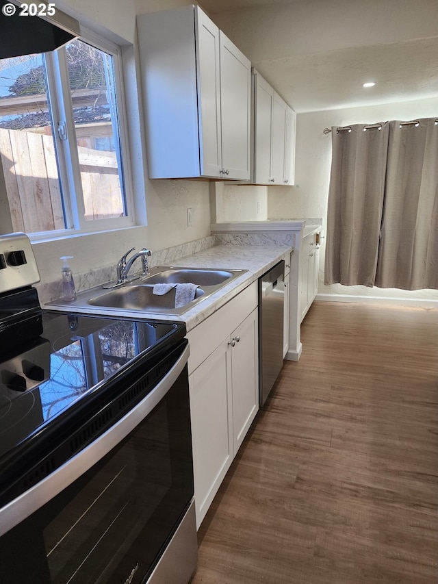 kitchen featuring wood finished floors, a sink, white cabinetry, light countertops, and appliances with stainless steel finishes