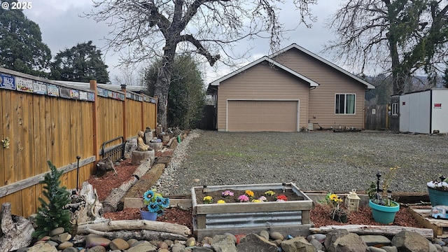 view of yard with a garage, gravel driveway, a vegetable garden, and fence