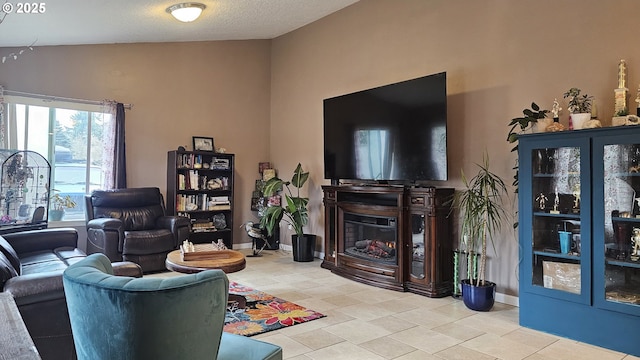 living area with tile patterned floors, a glass covered fireplace, a textured ceiling, and baseboards