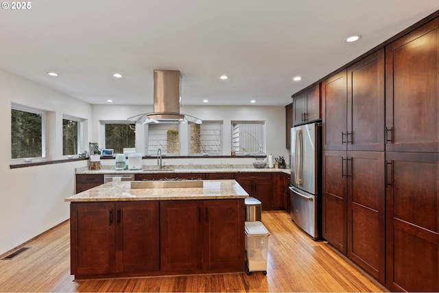 kitchen with a kitchen island, island range hood, light hardwood / wood-style floors, stainless steel appliances, and light stone countertops