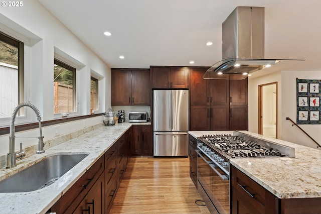 kitchen with light stone counters, stainless steel appliances, sink, and island range hood