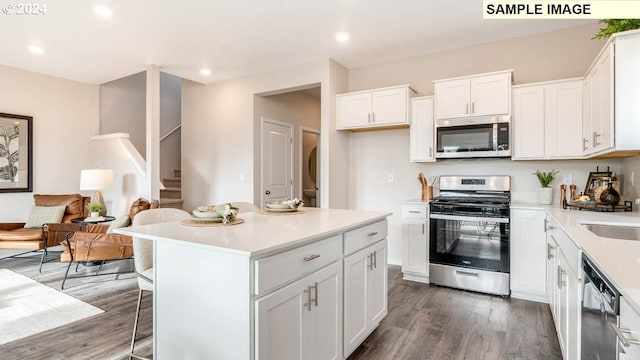 kitchen with appliances with stainless steel finishes, a center island, white cabinets, and dark hardwood / wood-style flooring