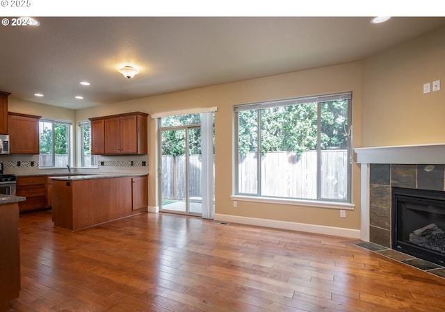 kitchen with stainless steel appliances, sink, a tile fireplace, hardwood / wood-style floors, and backsplash