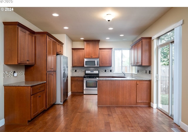 kitchen featuring light stone countertops, dark hardwood / wood-style flooring, tasteful backsplash, and appliances with stainless steel finishes