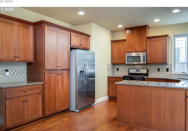 kitchen with stainless steel appliances, light stone countertops, decorative backsplash, and hardwood / wood-style floors