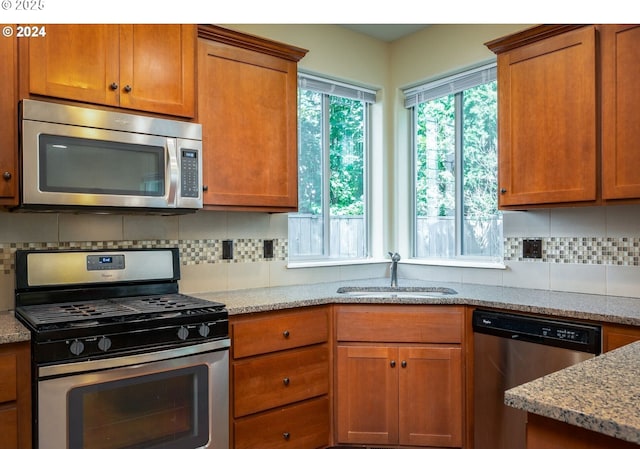 kitchen featuring light stone counters, stainless steel appliances, backsplash, and sink