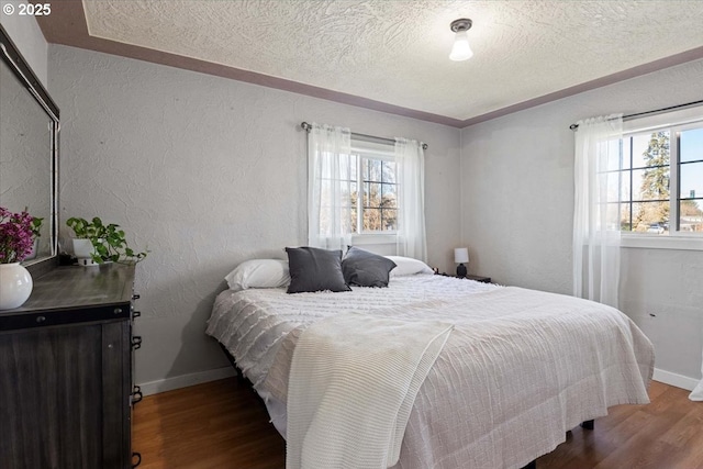 bedroom featuring a textured ceiling, baseboards, wood finished floors, and a textured wall