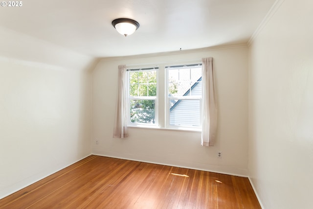 empty room featuring wood-type flooring, baseboards, ornamental molding, and vaulted ceiling