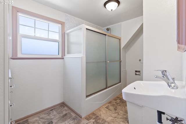 full bath featuring shower / bath combination with glass door, a sink, baseboards, and stone finish flooring
