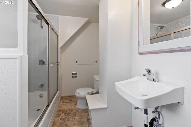bathroom featuring toilet, stone finish flooring, bath / shower combo with glass door, and baseboards