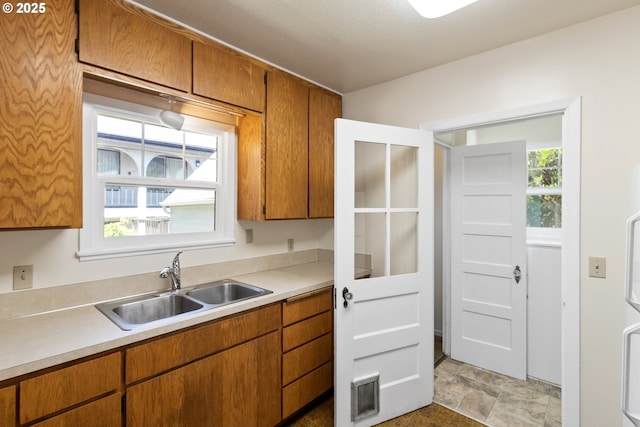 kitchen featuring a sink, light countertops, brown cabinetry, and stone finish floors