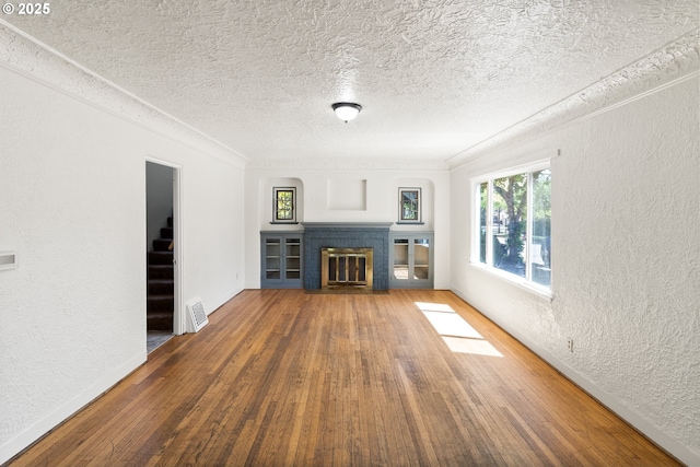 unfurnished living room with wood-type flooring, a fireplace with flush hearth, a textured wall, a textured ceiling, and baseboards