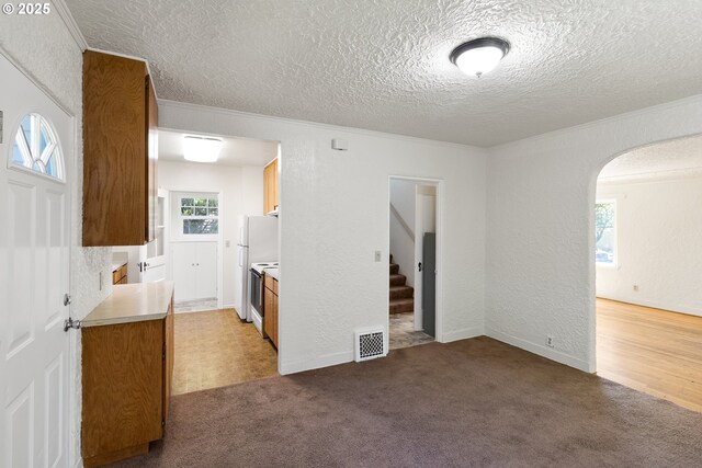 carpeted empty room featuring a textured ceiling, arched walkways, stairs, a textured wall, and ornamental molding