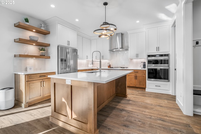 kitchen with white cabinetry, sink, wall chimney range hood, stainless steel appliances, and a center island with sink