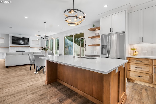 kitchen featuring sink, white cabinetry, a kitchen island with sink, stainless steel refrigerator with ice dispenser, and decorative light fixtures