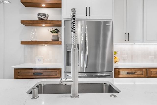 kitchen with sink, white cabinetry, light stone countertops, stainless steel fridge with ice dispenser, and decorative backsplash