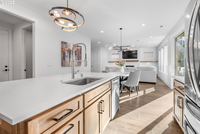 kitchen with pendant lighting, sink, stainless steel appliances, light brown cabinetry, and a chandelier