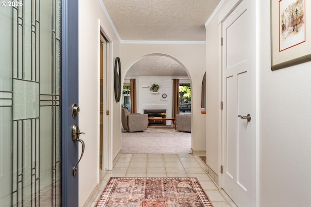 hall featuring ornamental molding, light carpet, a textured ceiling, arched walkways, and light tile patterned floors